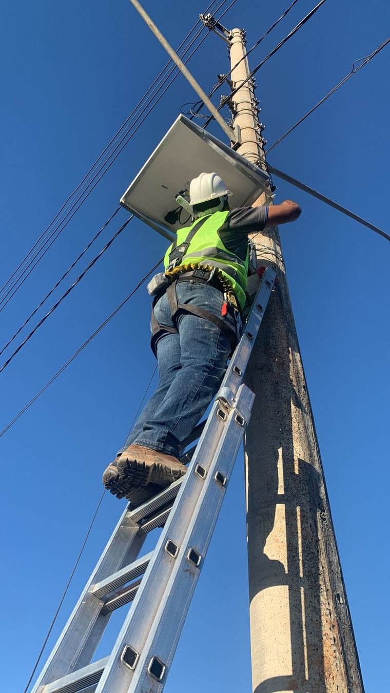 Técnico com equipamento de segurança instalando câmera Synvix em poste